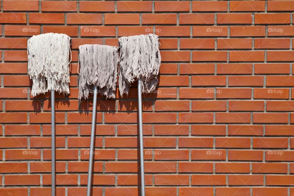 Three mop lean against red brick wall