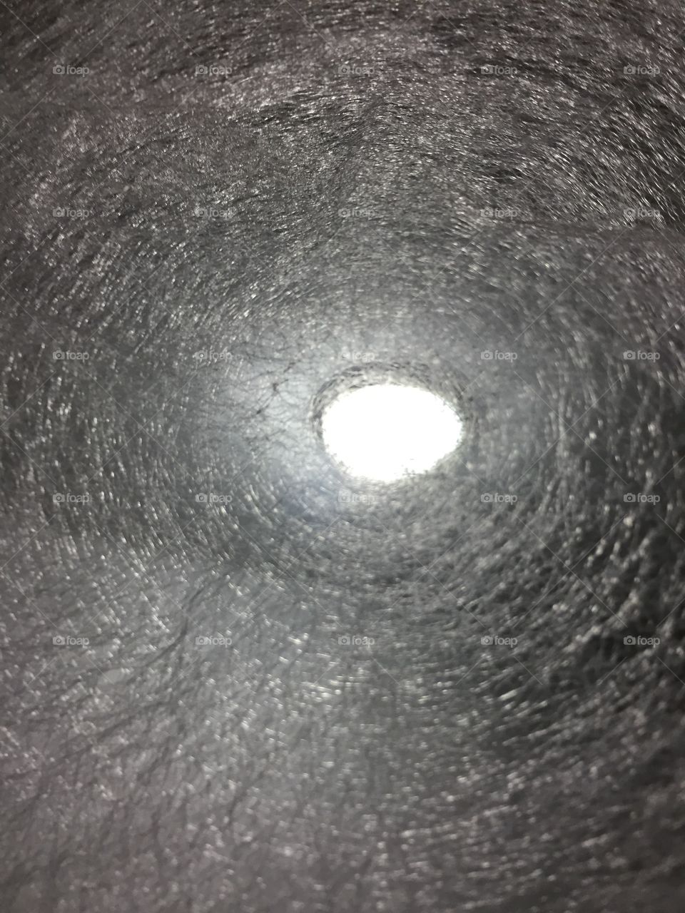 Silvertone abstract with light shining through a circular hole in the middle. 