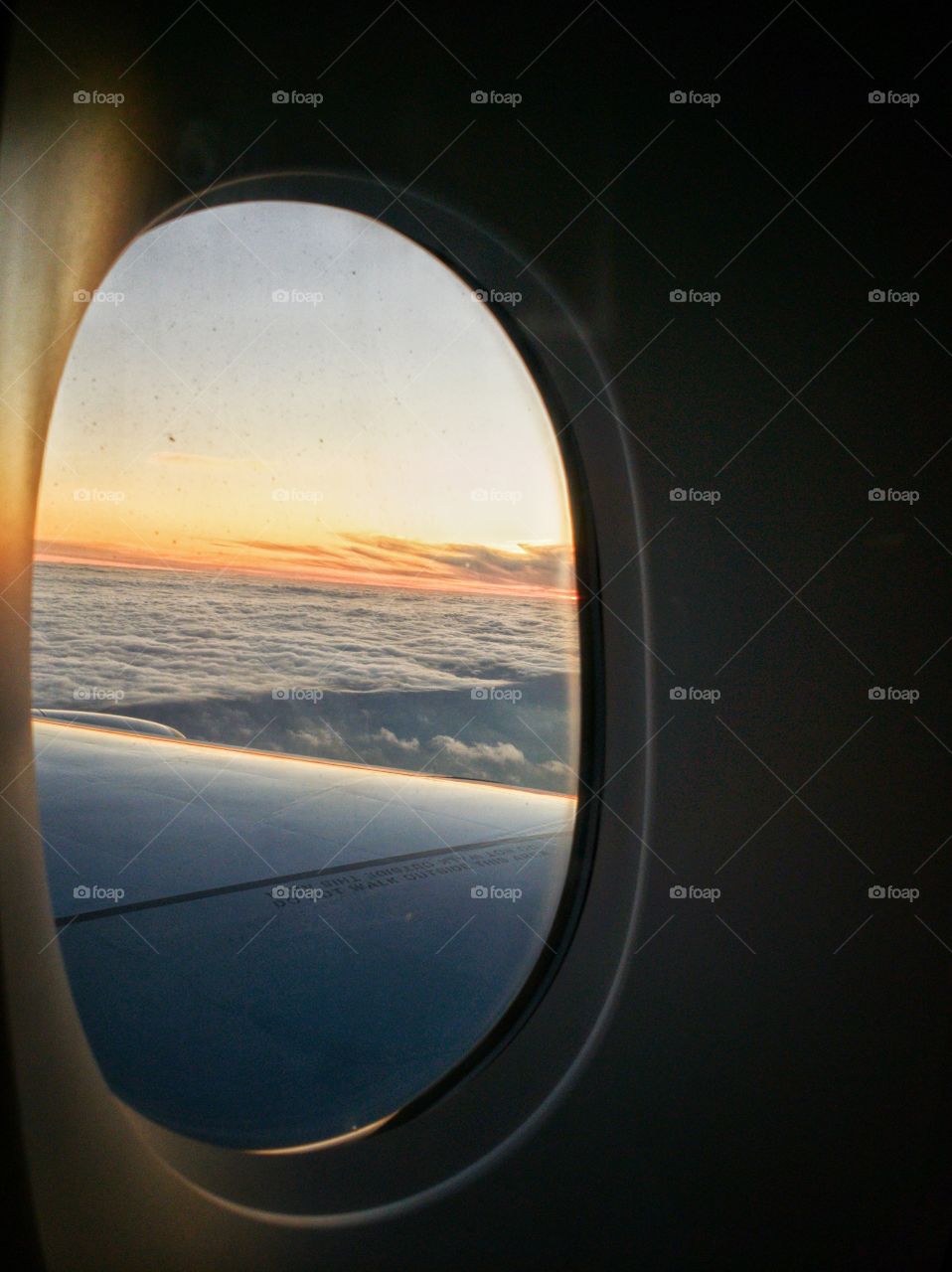 Onboard airplane looking out the window in the setting sun as it flies just above the clouds. Sunset colours.