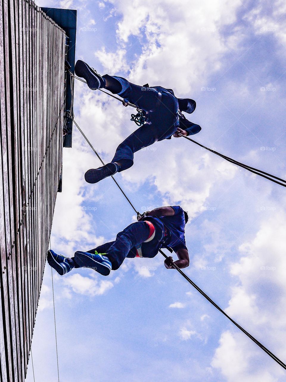 Two people climbing the outdoor tower against blue sky