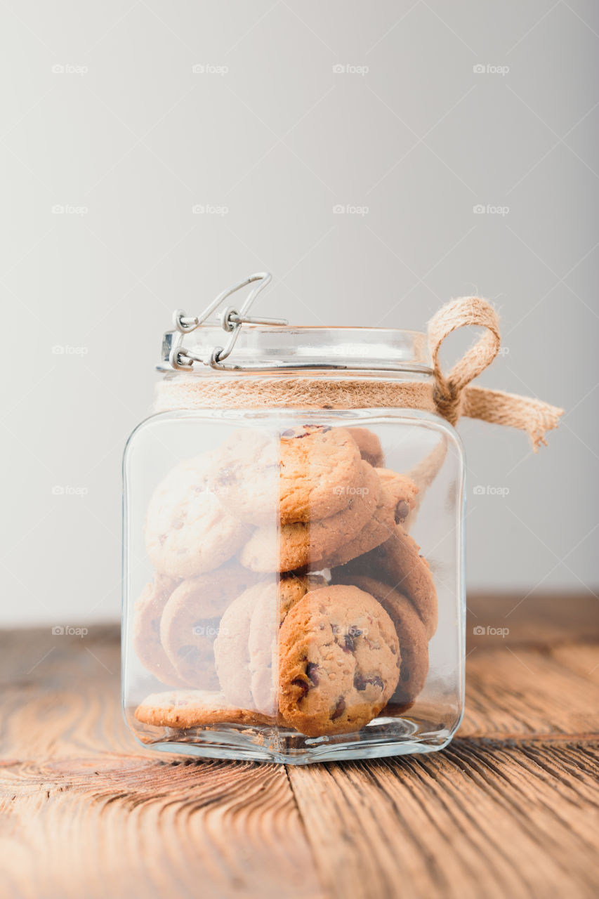 Big jar filled with oat cookies standing on a wooden table. Plain background. Portrait orientation