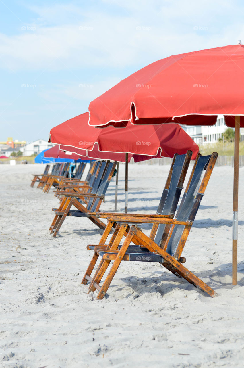 Vertical image of a row of empty lounge chairs in the sand on the beach 