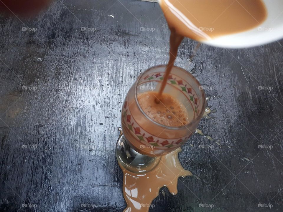 a cup of mocha coffee that was being poured but spilled over a small glass in the morning
