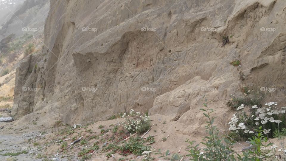 Carvings in a cliff face. Hearts, symbols, initials on a beachside cliff.