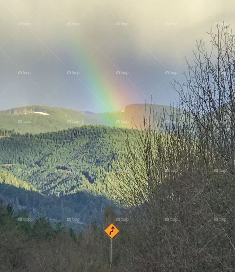 End of a rainbow and sunshine on green hills with traffic sign arrow pointing at it 