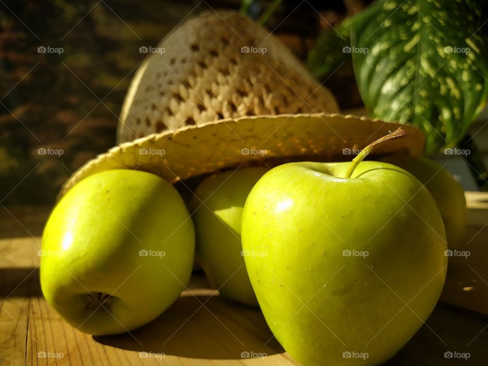 The sunbeam falls on green apples, which are covered with a straw hat
