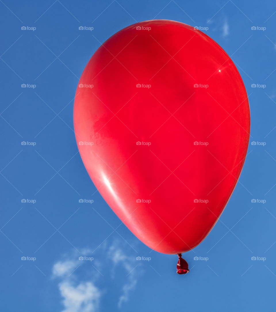 Vertical photo of a bright red balloon floating against a blue sky with small white clouds