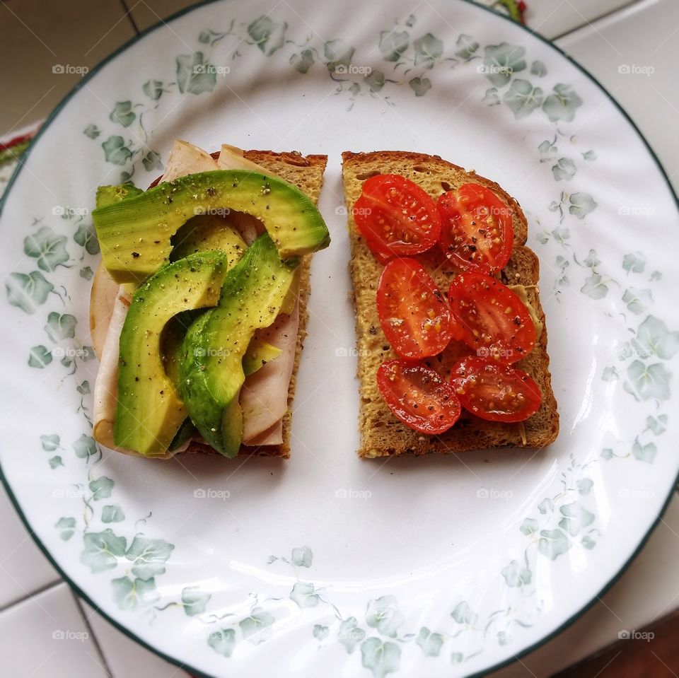 Turkey avocado tomato dijon mustard on whole grain wheat bread sandwich on a plate