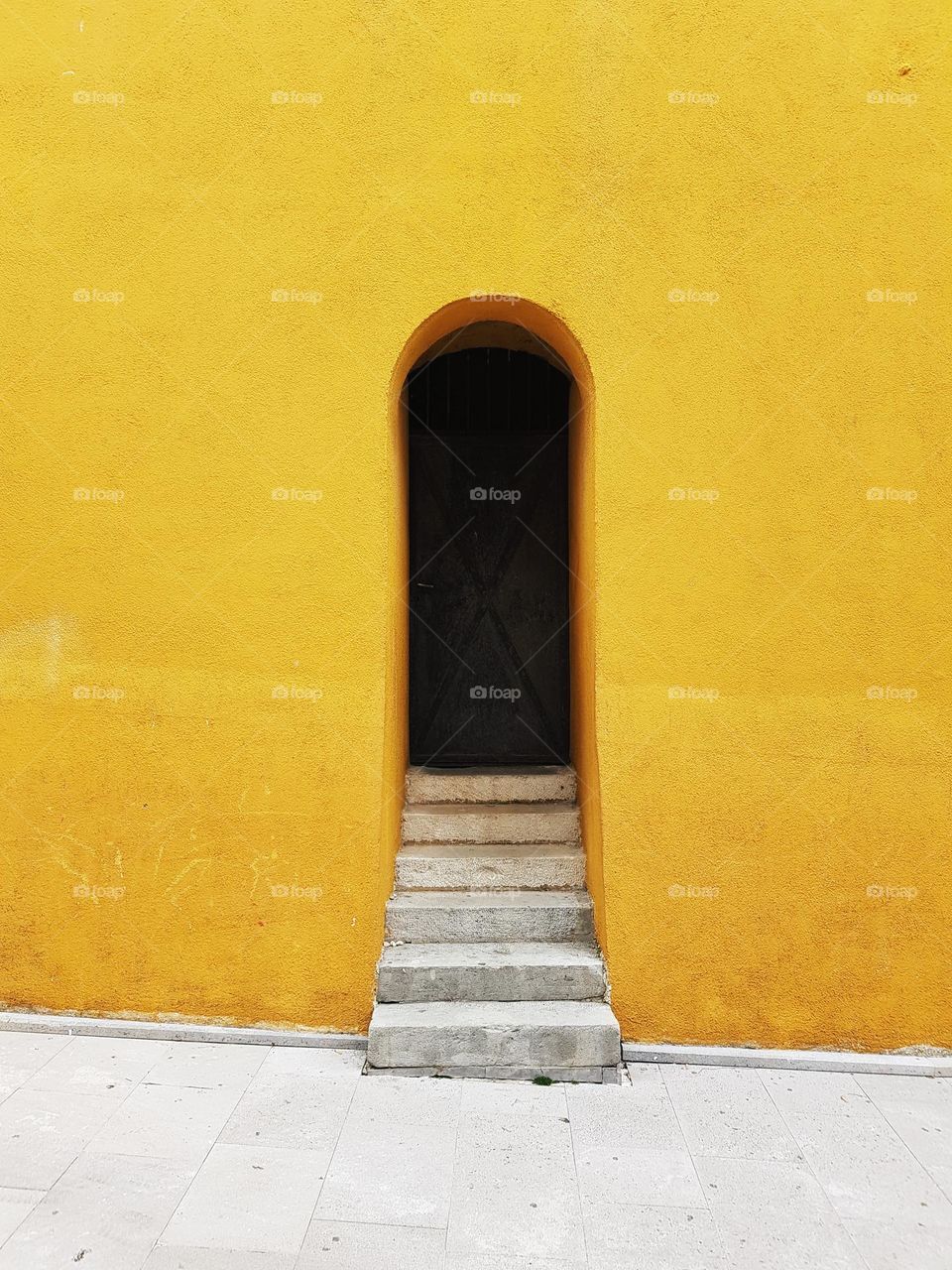 Minimalist photo of stairs leading to dark door on yellow wall