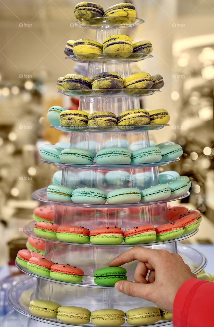 Person reaching for a colorful macaron from a display shaped like a Christmas tree - sweet holiday foods