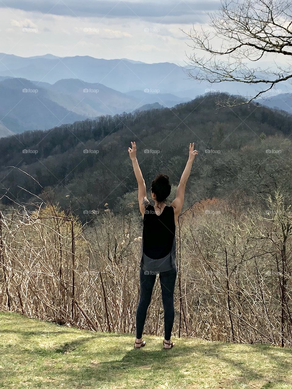 The back of a young woman who is facing the mountains in Tennesee with her arms raised in the air. 