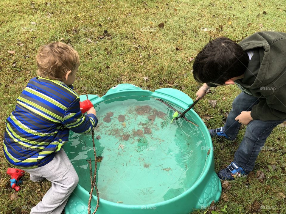 Two little boys with sticks playing fishing in a rain water filled pool