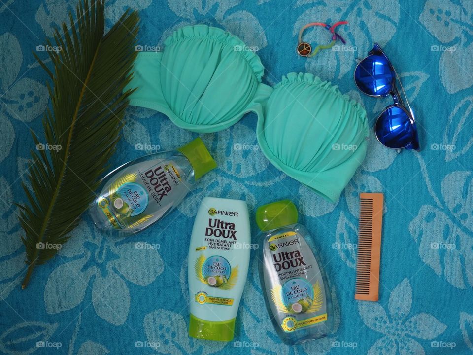 Garnier eau de coco shampoo, conditioner and bath gel on a blue towel with comb and palm leaf and blue sunglasses and bikini.