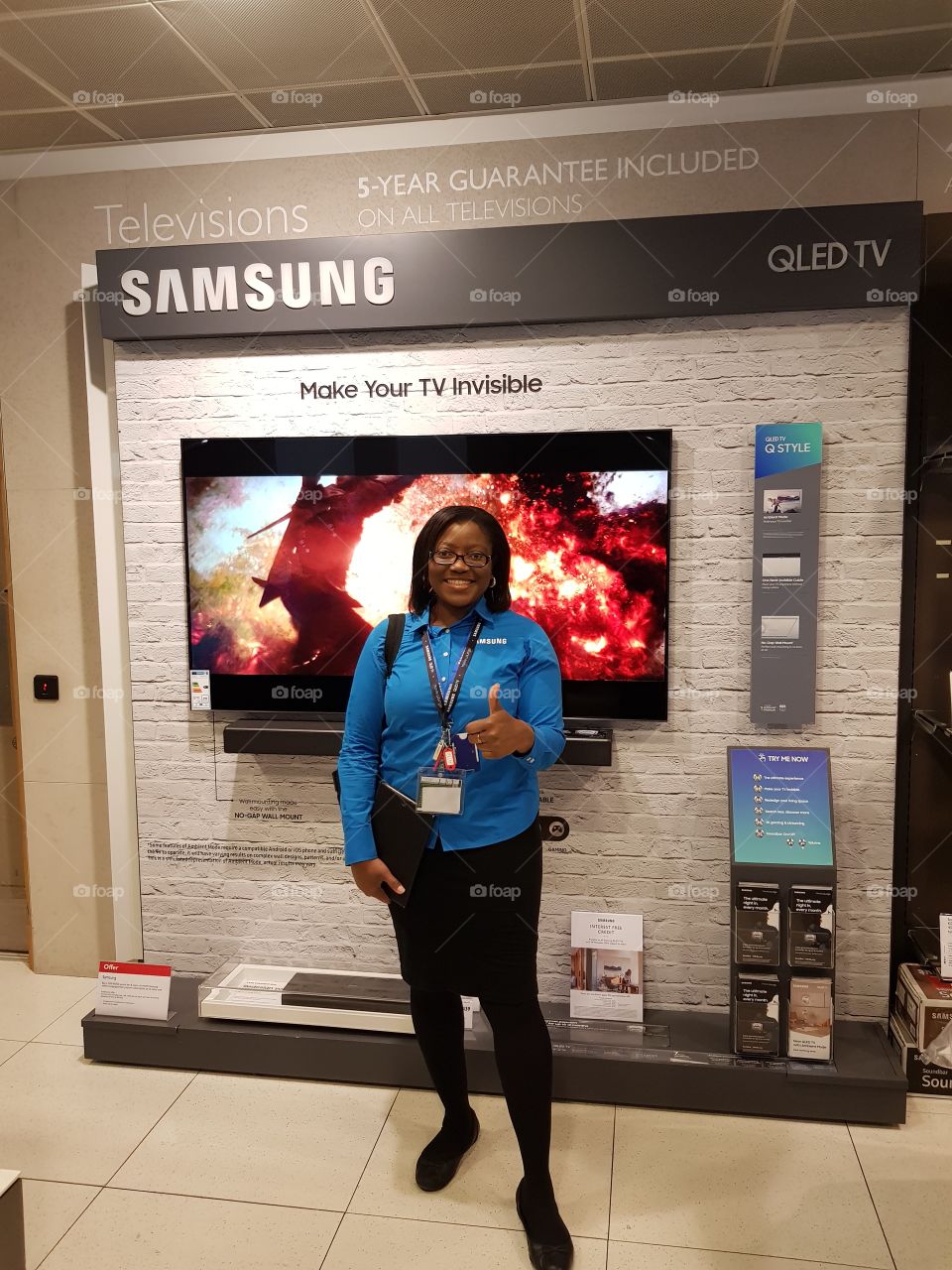 Samsung field force posing in front of the Samsung wall mounted QLED television with soundbar and one connect box with fibre optic cable