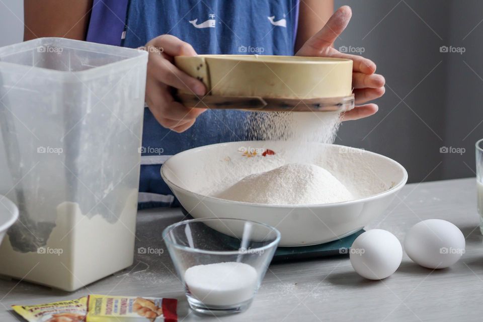 Child is sifting flour for cooking