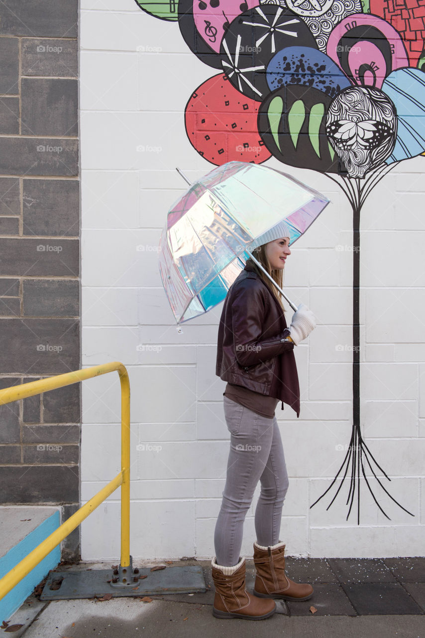 Young woman holding an umbrella while walking on a sidewalk in front of a colorful mural