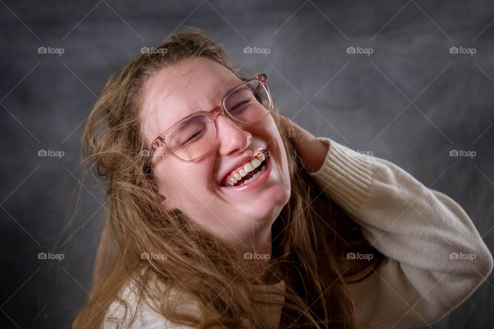 A young lady with glasses is near tears from laughter. 