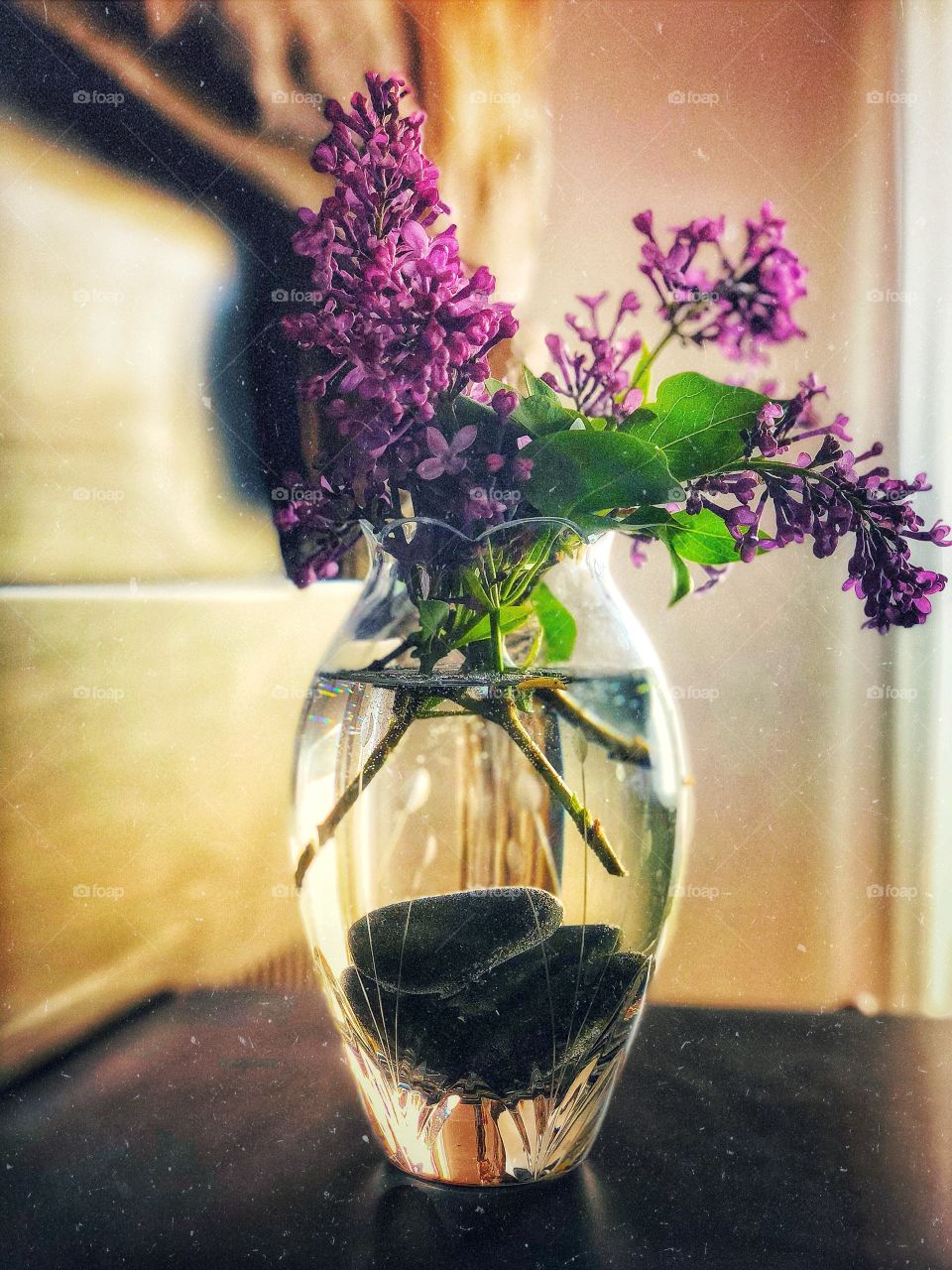 Lovely lilacs in a glass vase filled with rocks, shimmering light behind