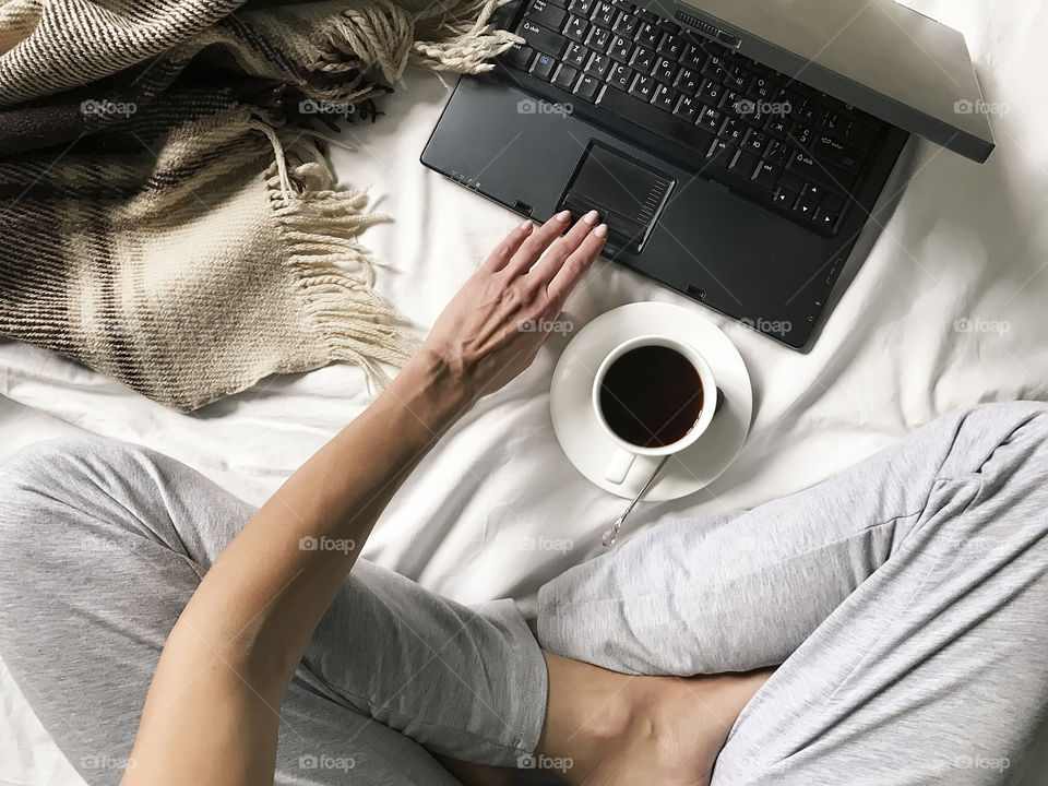 Drinking coffee and using laptop in cozy bed 