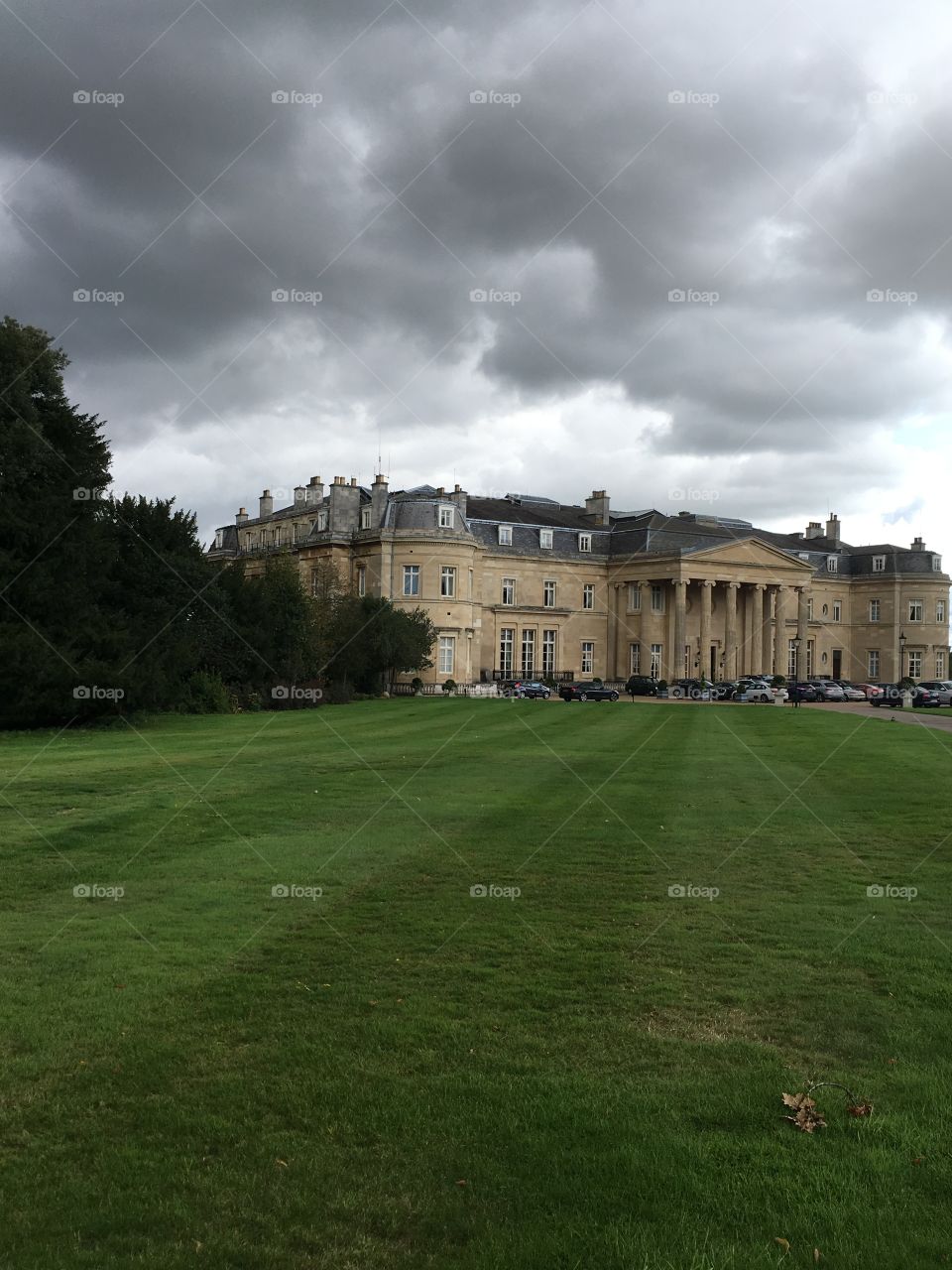 The Luton Hoo estate taken on a stormy day in England. A large yard with green grass and the mansion is all the way in the distance, next to some trees