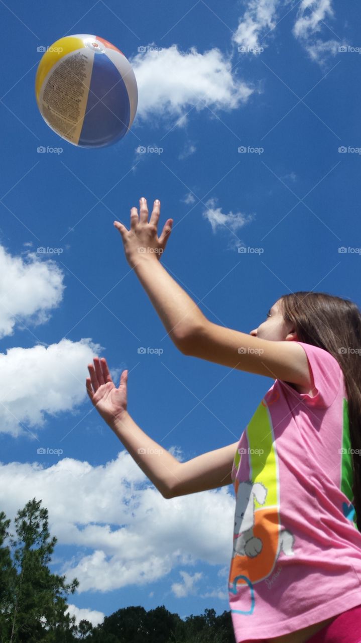 Girl catching beach ball in blue sky