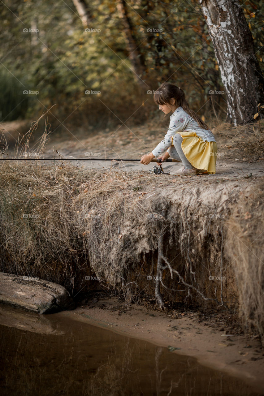 Little girl fishing on a lake at autumn day 