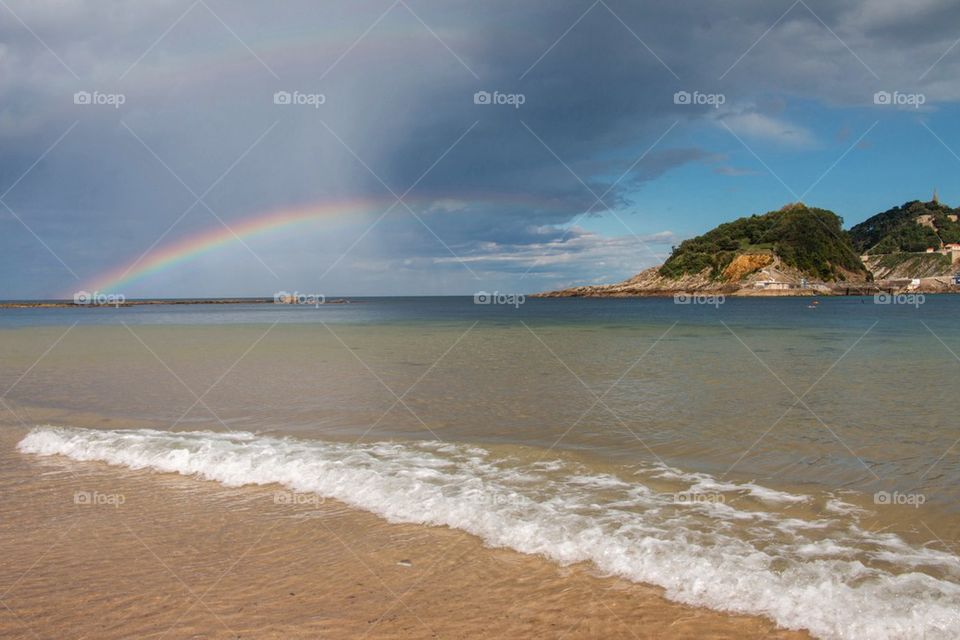 Rainbow over sea against cloudy sky