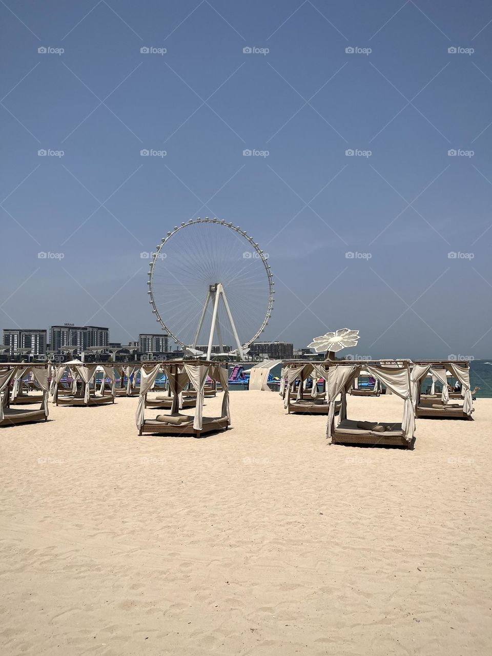 View of a Dubai beach with canopy beds on the sand and a Ferris wheel in the background
