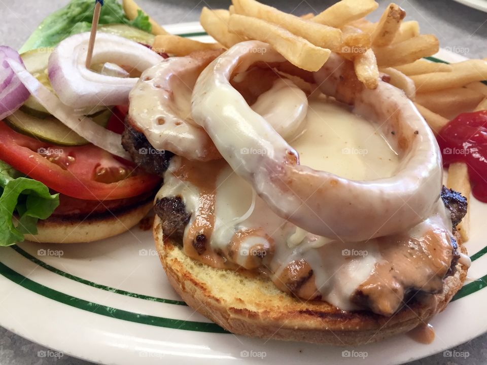 A cheeseburger with lettuce, tomatoes and onion served on a toasted roll with a side of french fries at a diner