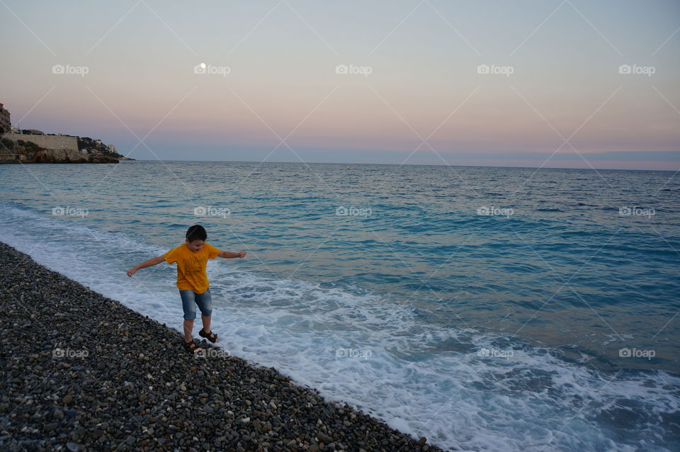 Boy walking on the pebbles of the azure shore