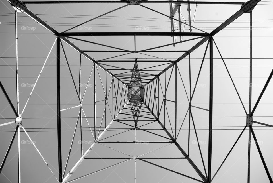 A vertical ground level perspective through the steel mazery of a high tension electric tower.