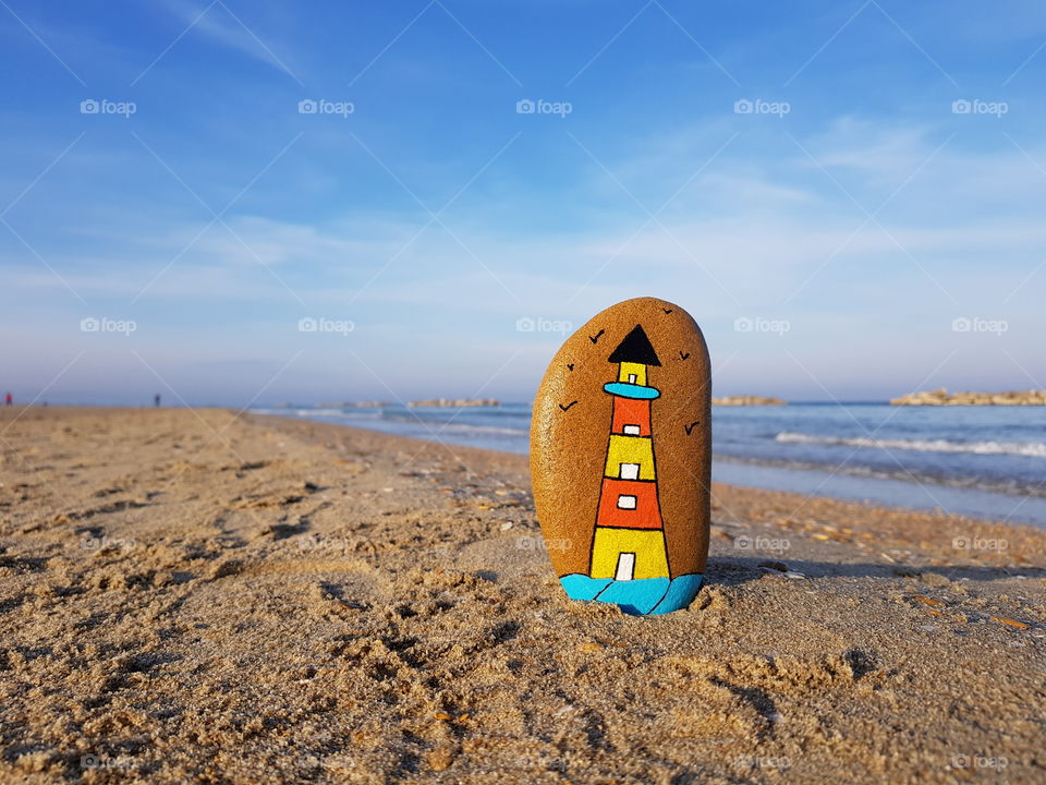 Lighthouse concept painted on a stone with beach background