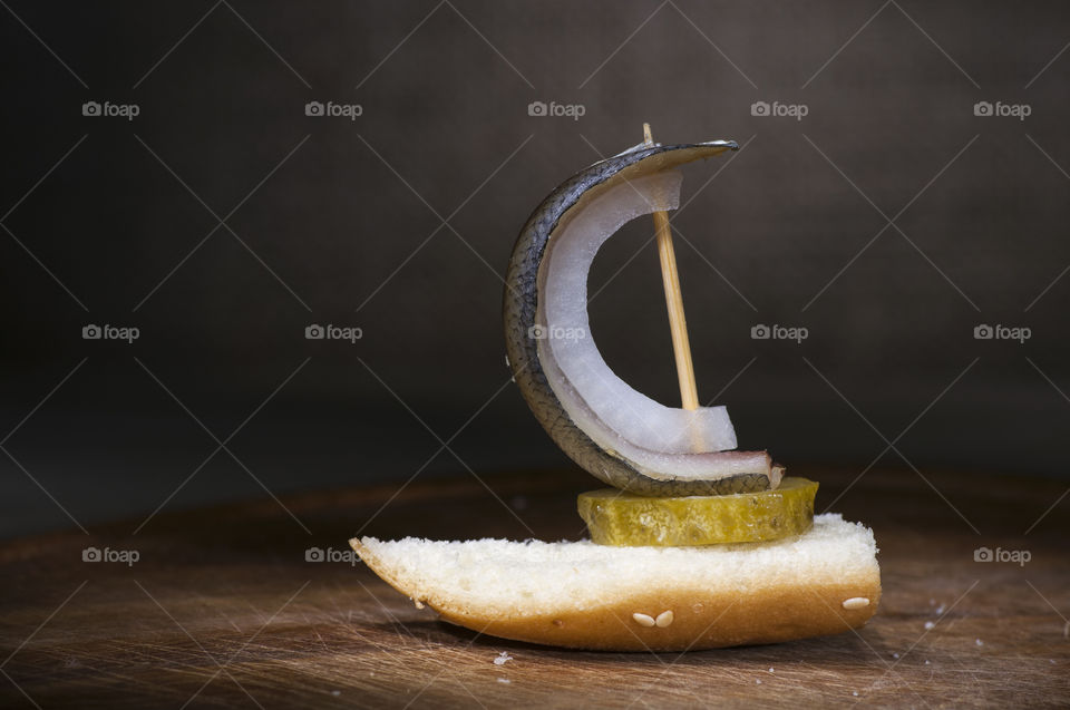 Canape made of salted herring, onion, baguette and pickled cucumber close up