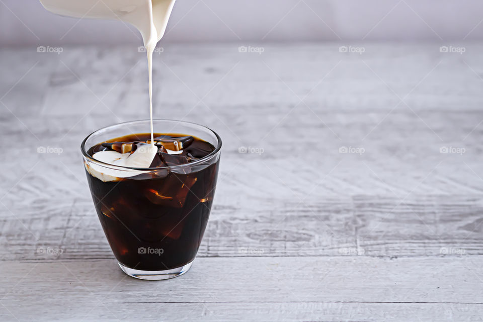 Cream poured in the glasses with coffee and ice cube on the wooden table. Copy space.