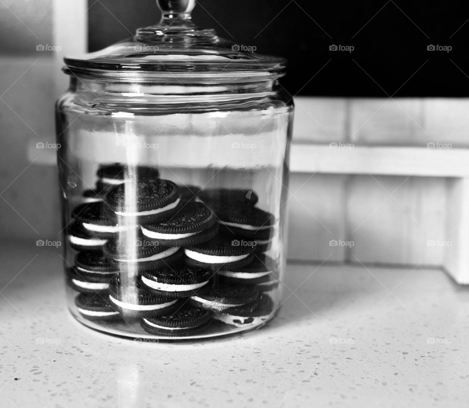 Black and white photo of chocolate sandwich cookies in a  glass jar on a counter 