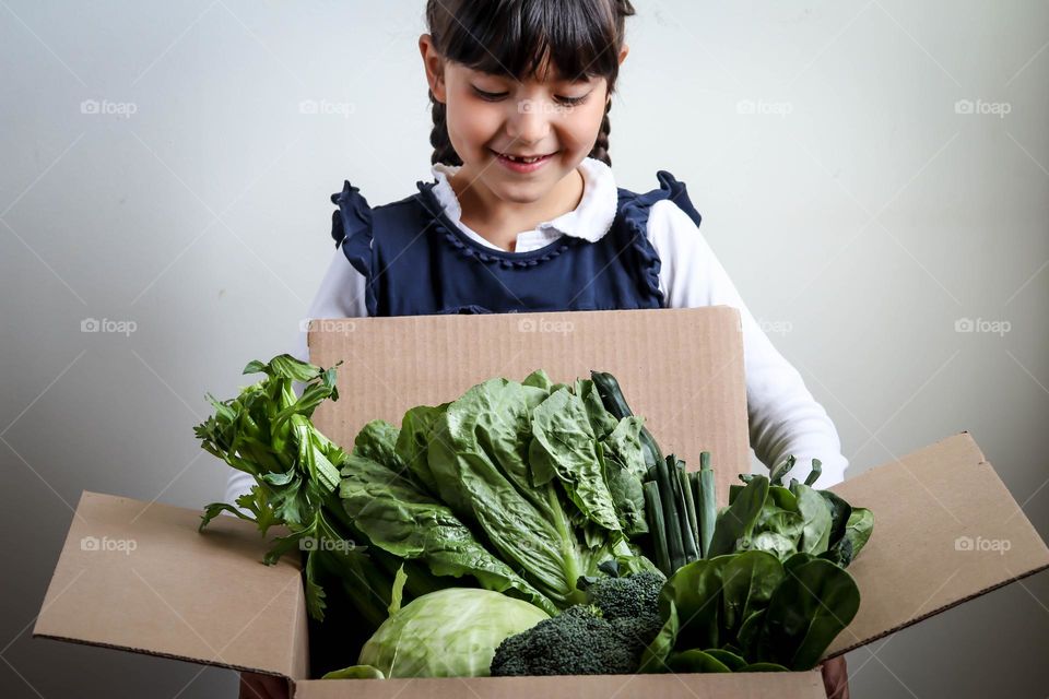 Happy cute little girl with a cardboard box of green vegetables