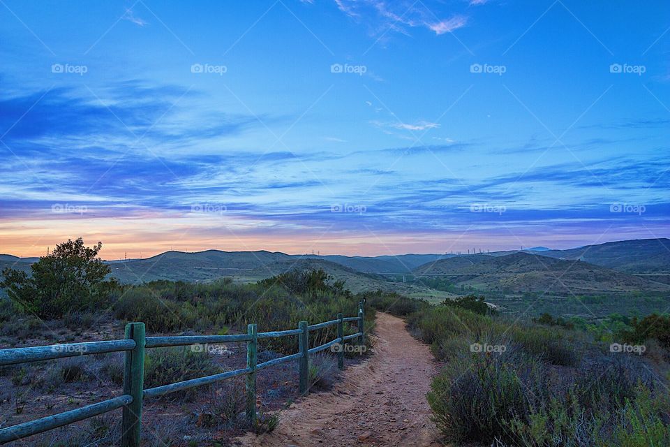 Mountaintop view with trail and wooden railing at sun down