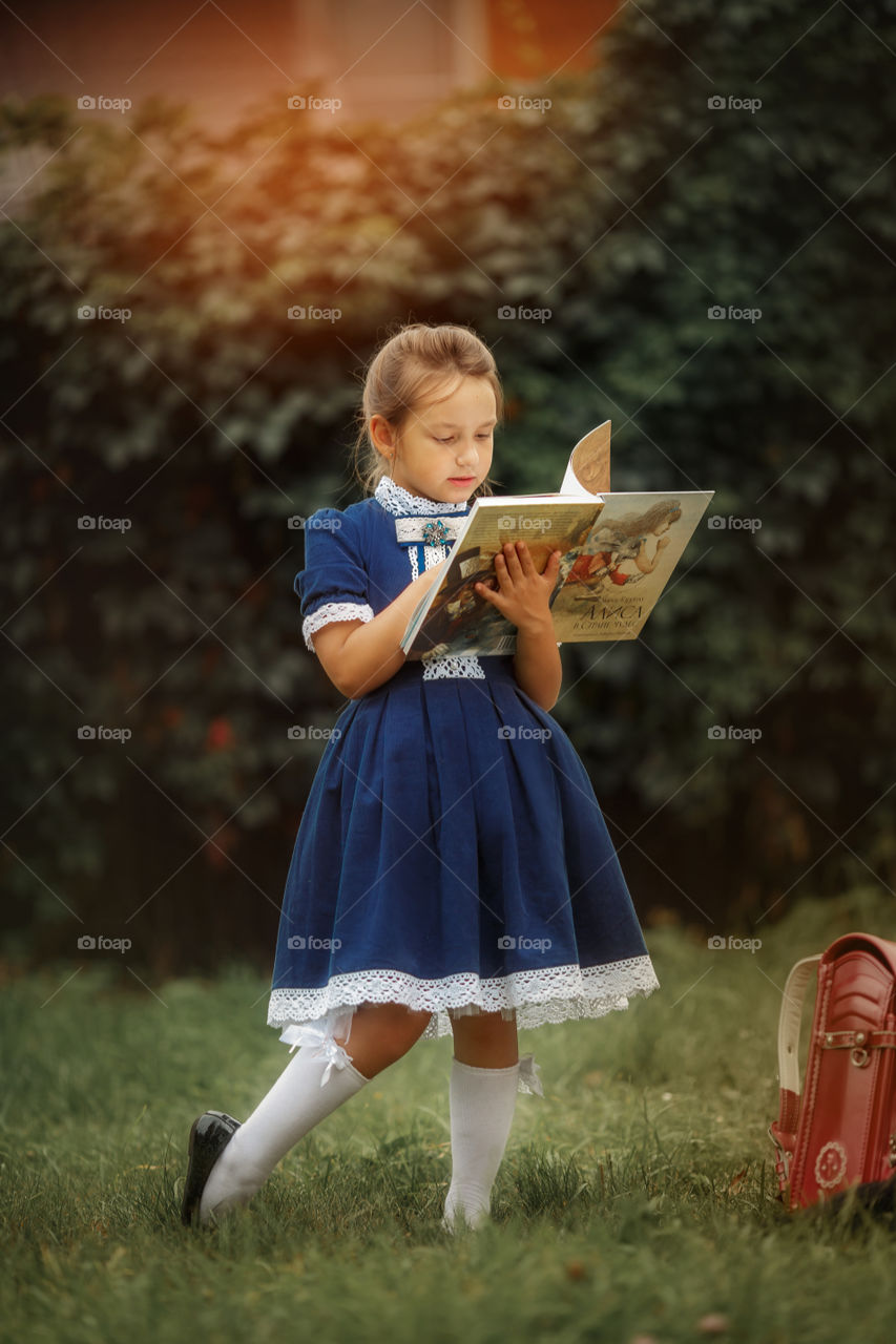 Little schoolgirl with a book at a park 