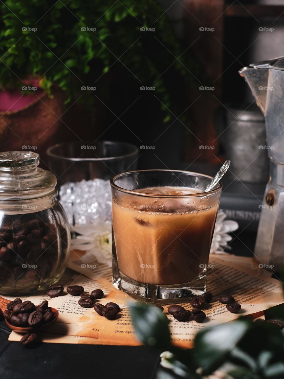 Summer drink iced coffee in glass and coffee beans in glass jar on dark background.