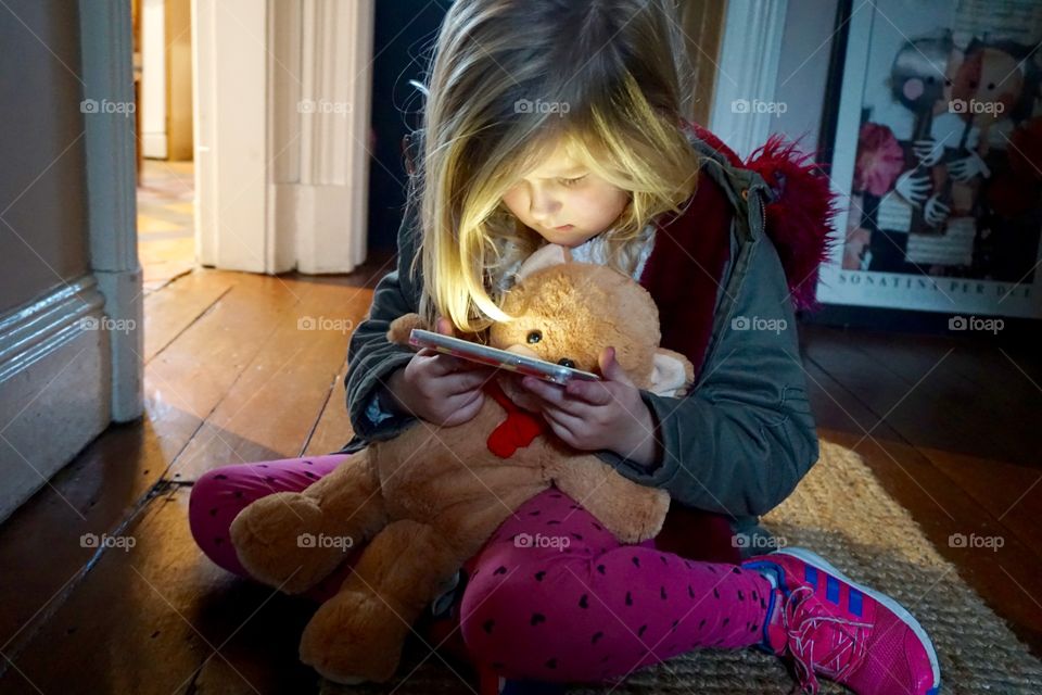 Girl holding teddy bear looking at cellphone