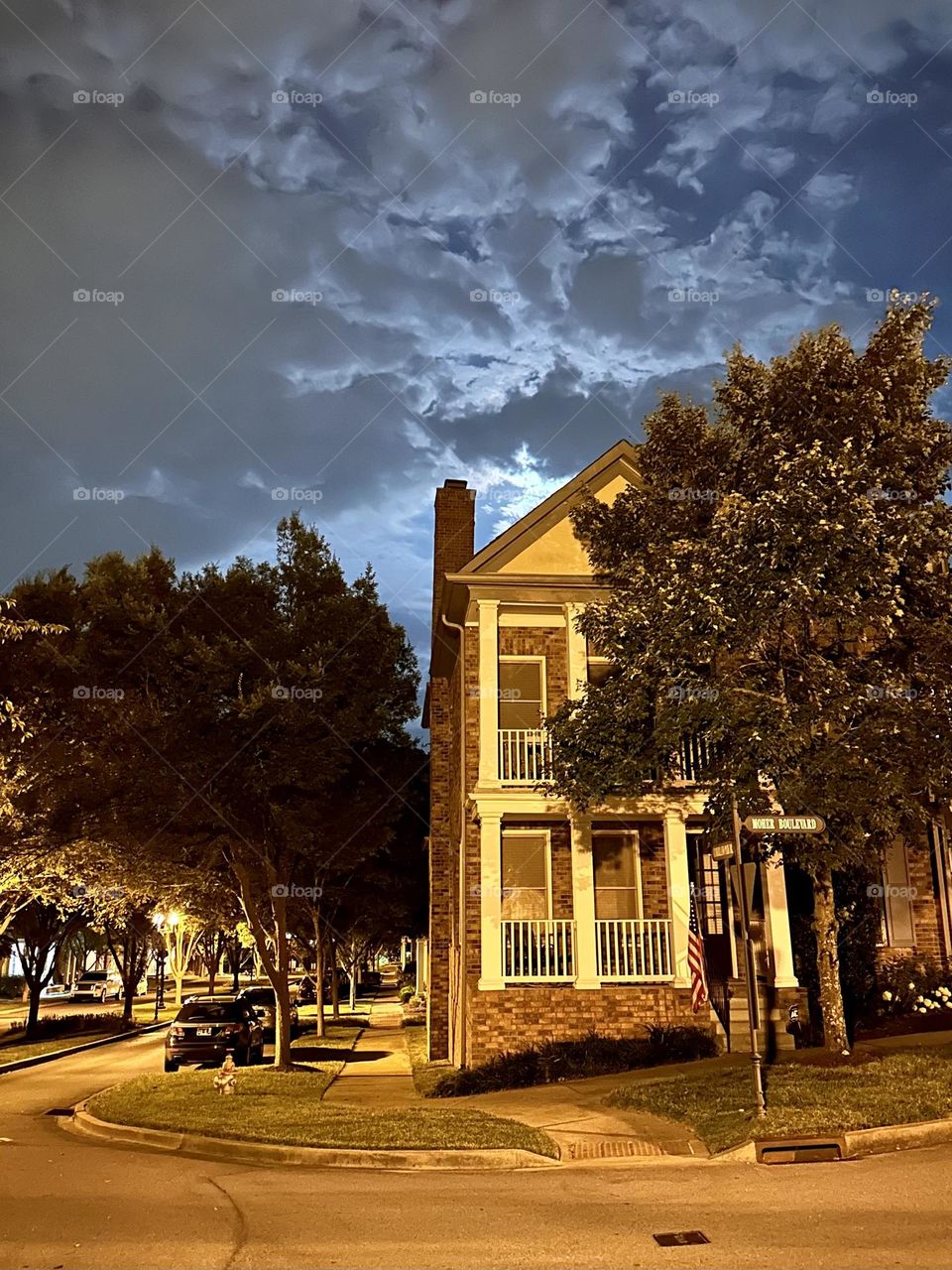 Neighborhood house at night with cool moon sky clouds suburban landscaping and cars parked along street