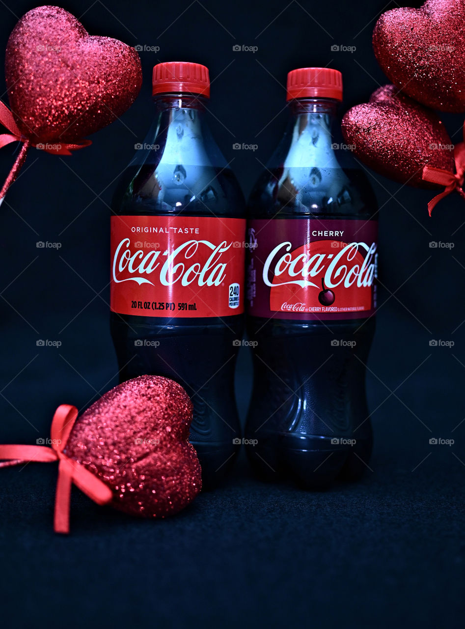Close up shot of two Coca Cola with black background with the mists at the studio with hearts. 