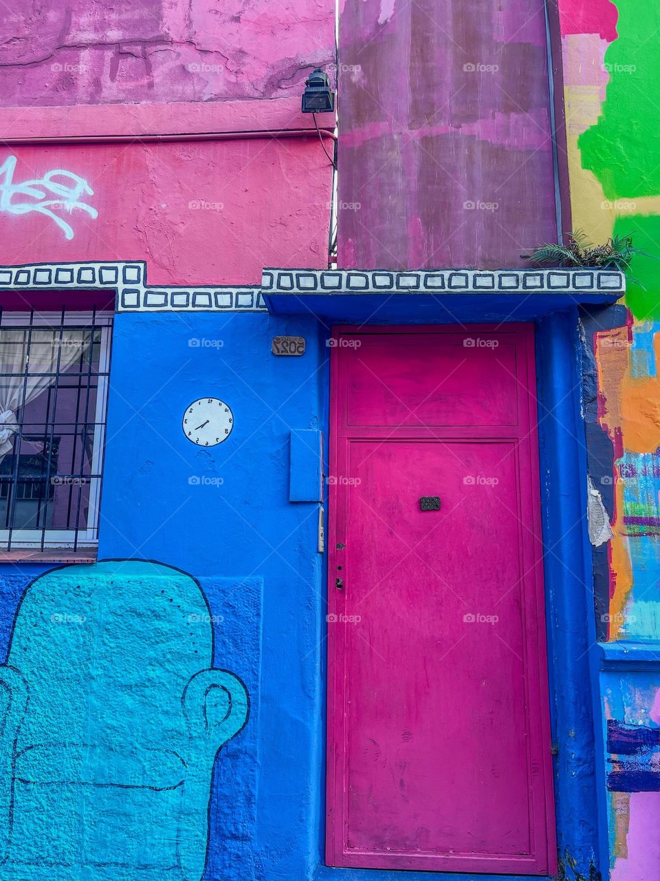 A vibrant pink door on a wall full of urban art, standing out amid shades of blue and a large stylized sofa painting. The image conveys a feeling of creativity and joy, capturing the essence of modern urban life with bold textures and colors.