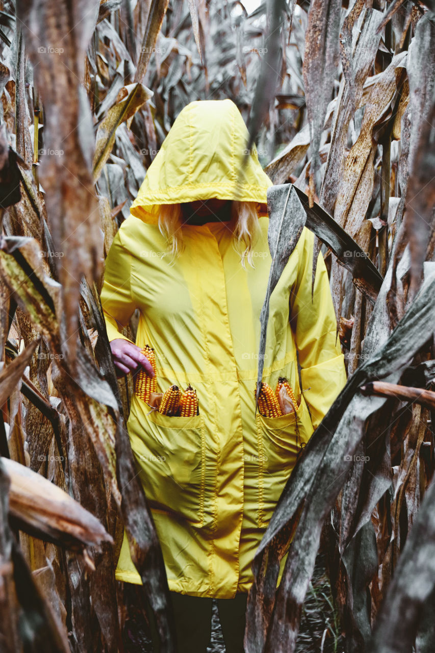 Woman with full pockets with corn cobs in the middle of cornfield 