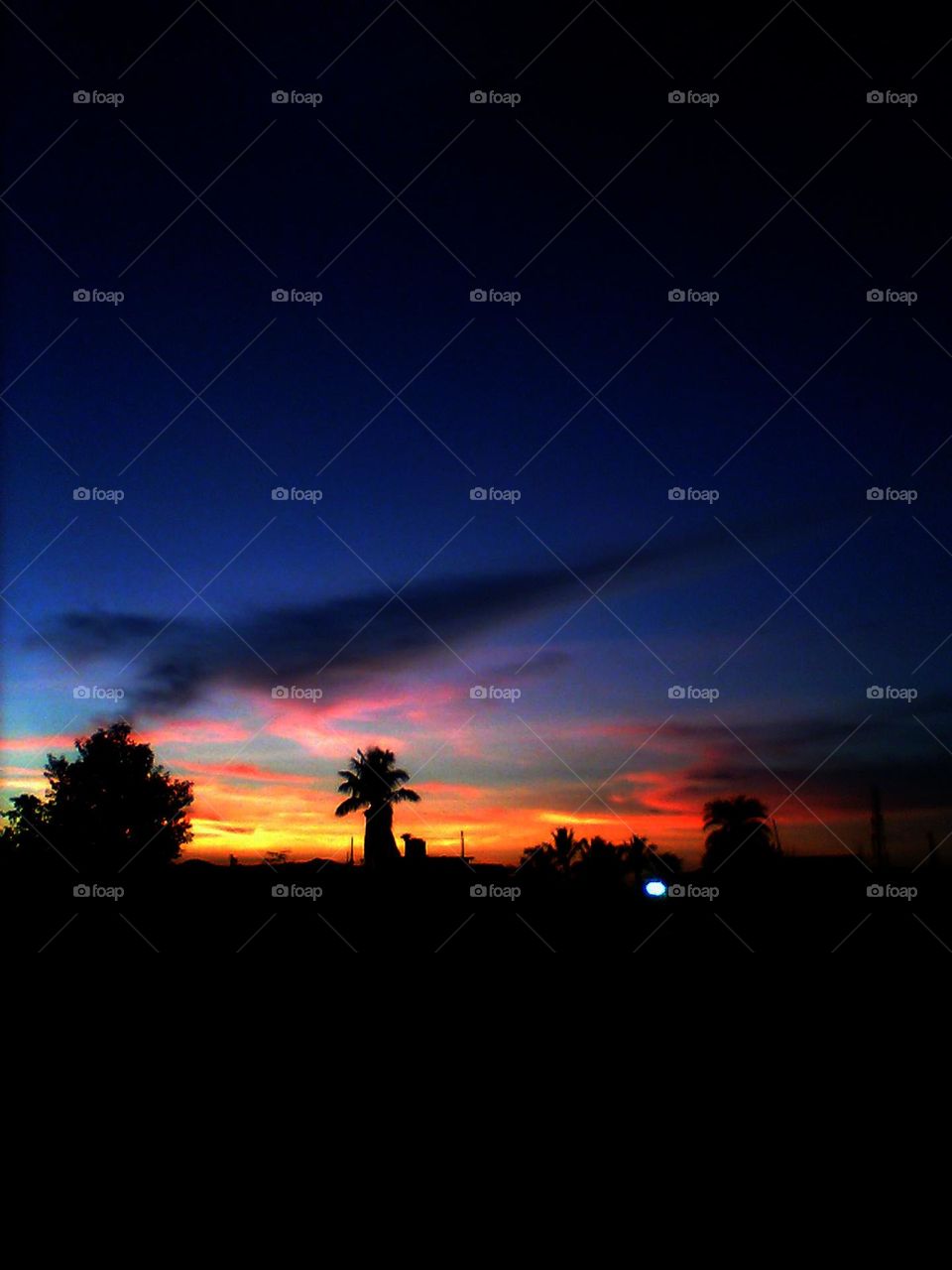 Vibrant orange and reddish clouds are set ablaze across the sky, casting a warm glow over the landscape. Deep black shadows stretch across the ground, creating a dramatic contrast to the fiery hues above. Wonder and awe at the breathtaking sunset.