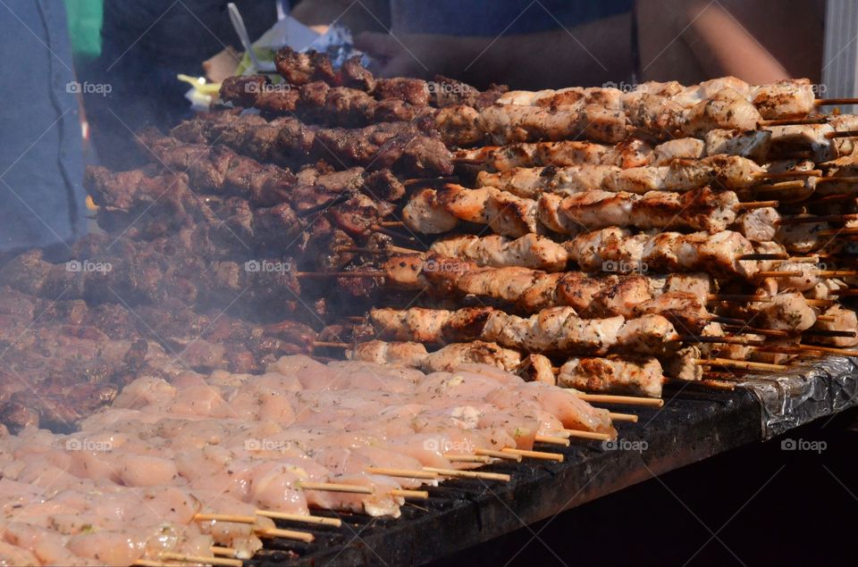 Sausage and chicken kebabs cook up on a grill at a street fair.
