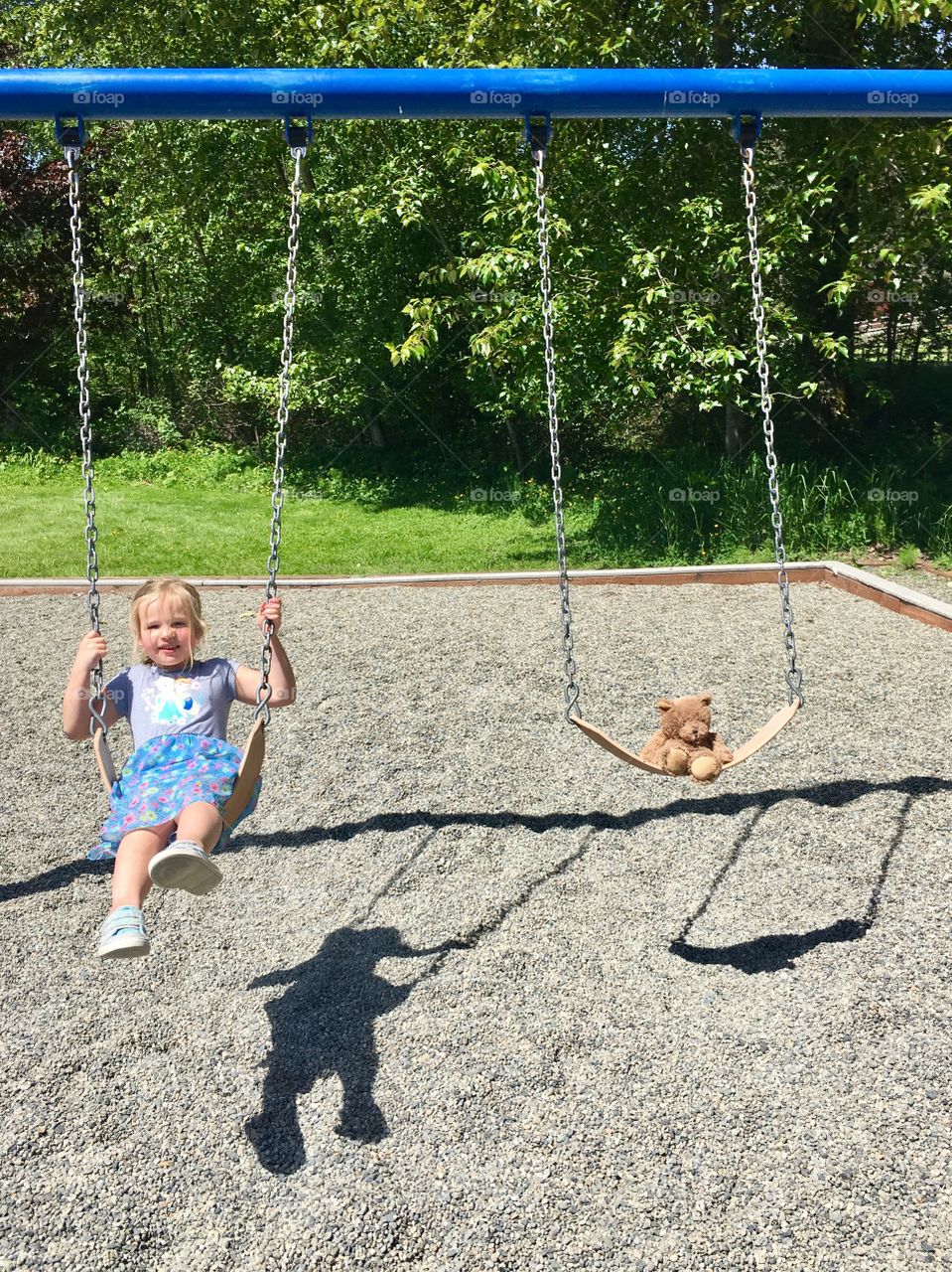 Little girl and teddy on swing in park 