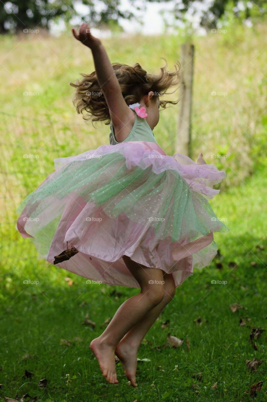 Toddler child in a frilly dress dancing outside. Hair is wild and she is in mid spin.