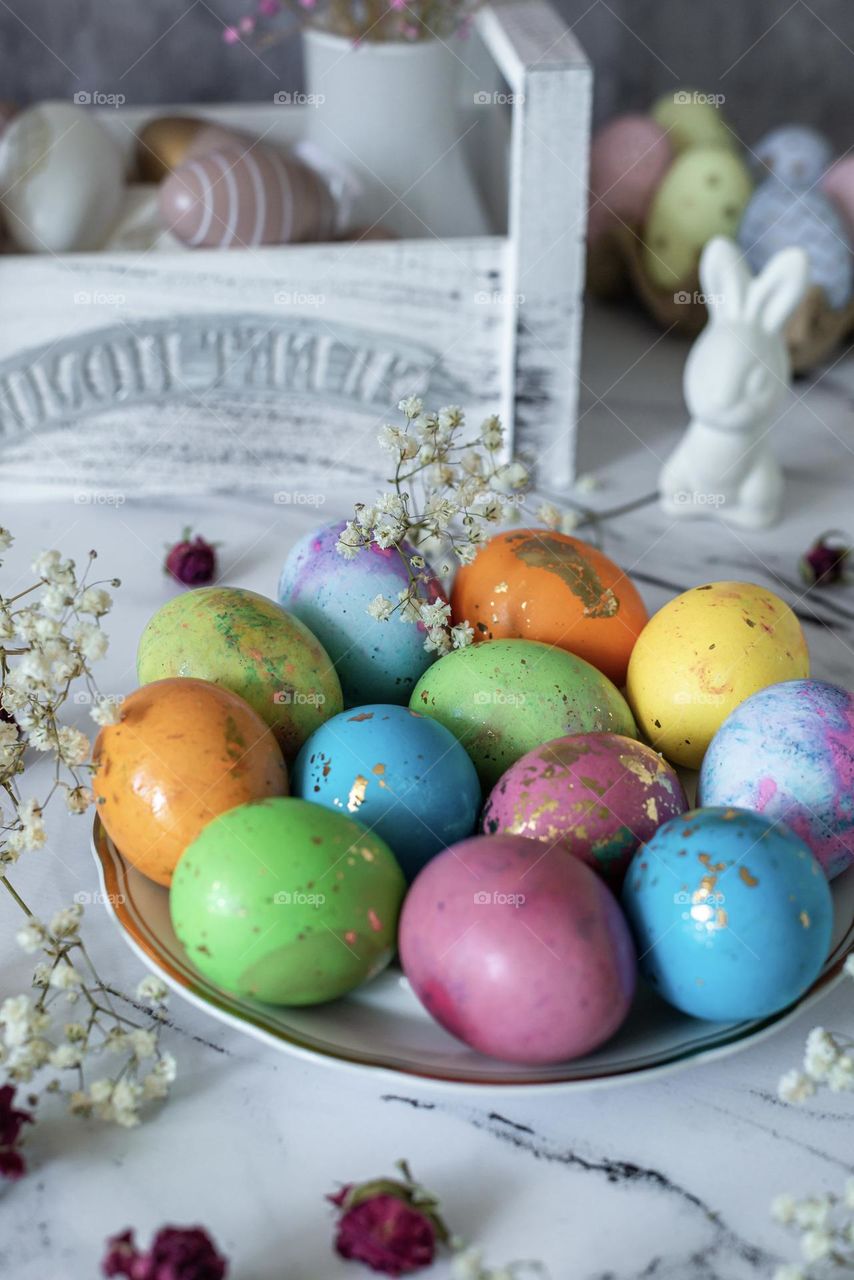 Still life on the table painted colored Easter eggs and a white rabbit, flowers 