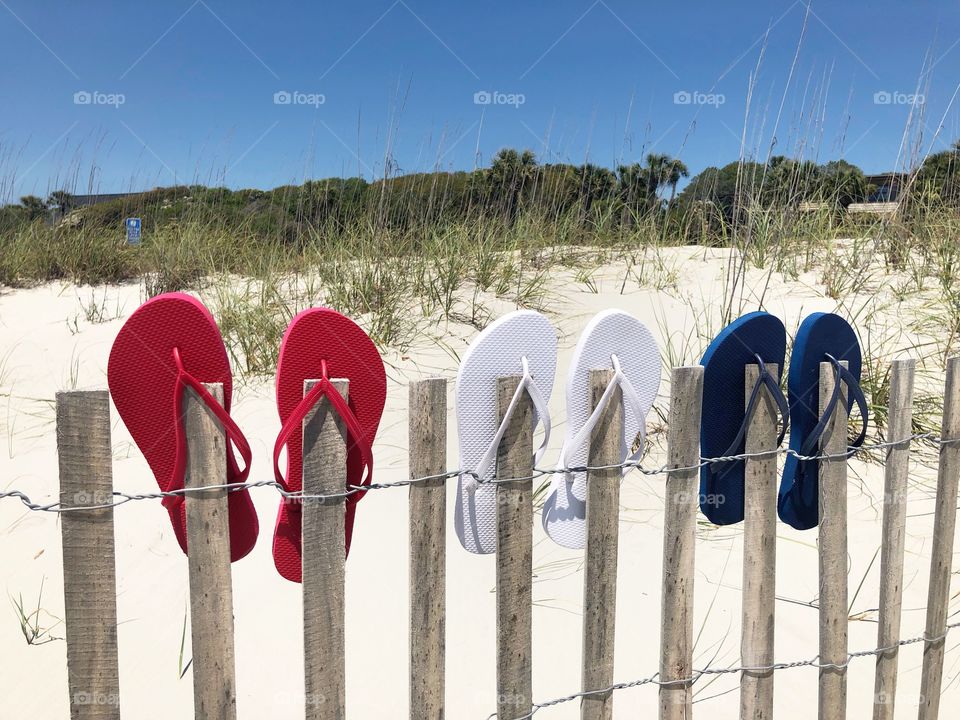 Red white and blue flip-flops on a beach fence.